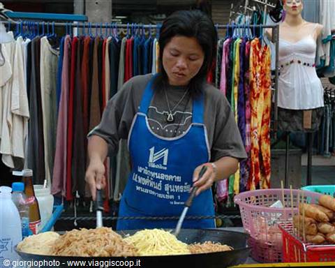 Vendor in blue apron cooks noodles in a wok at the market