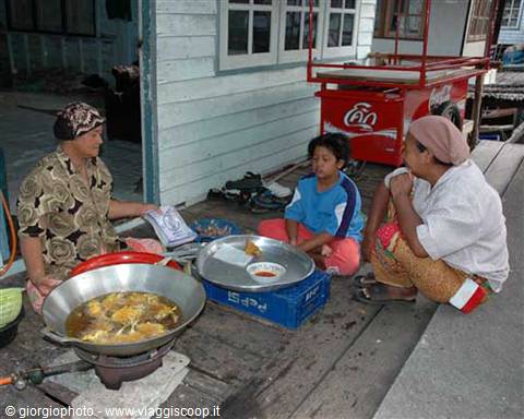 Women frying food in a wok outside their wooden stilt house