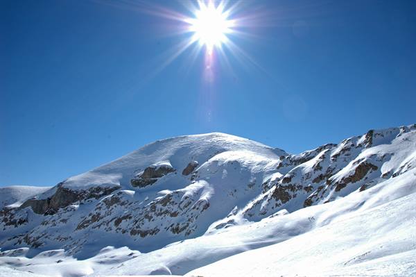 Shining sun over snowy peaks and rocks beneath blue sky