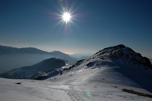 Bright sun over snowy ridge, ski slopes and misty mountains below