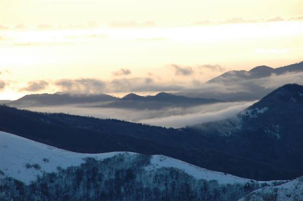 Snowy mountains among clouds under a peach-colored dawn sky