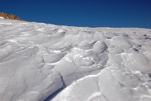 Wind-sculpted snow on an alpine slope, rock outcrop at left