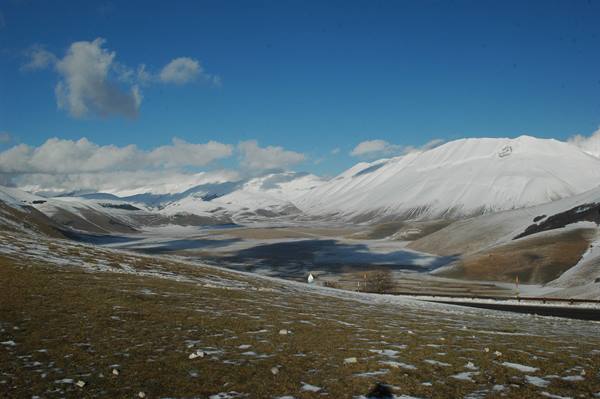 Snow-covered Castelluccio plain, white mountains under blue sky with clouds