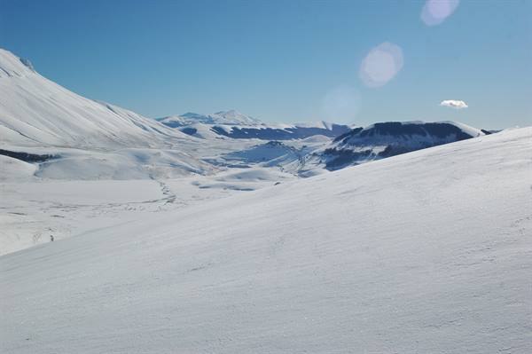 Snow-covered mountains and white slopes under a blue sky in Castelluccio di Norcia