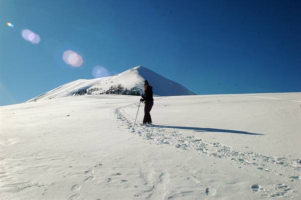 Skier with poles climbs across pristine snow toward a snowy peak, blue sky