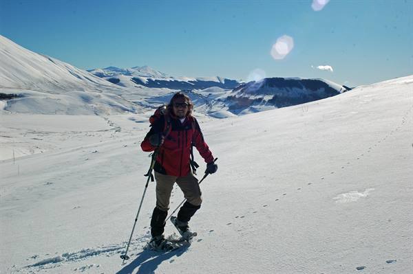 Hiker in red jacket with snowshoes and poles on a snowy mountain