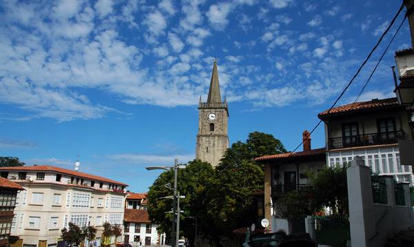 Stone bell tower with clock among red rooftops and traditional houses