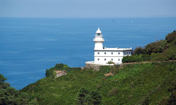 White lighthouse on green hill, blue sea behind, Japan