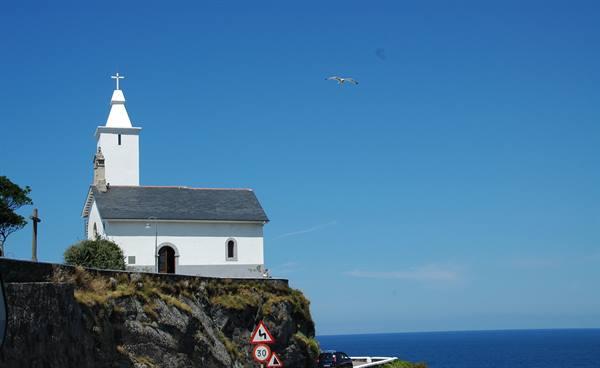 White hermitage with bell tower on rocky cliff overlooking the ocean, seagull flying