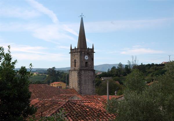 Stone bell tower with clock above tiled rooftops, green hills in background