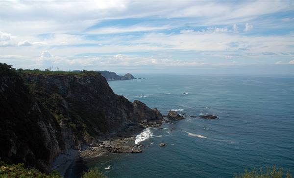 Rocky cliffs plunge into the blue sea, waves breaking on rocks
