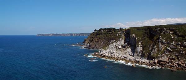 Rocky cliffs battered by blue waves under a clear sky