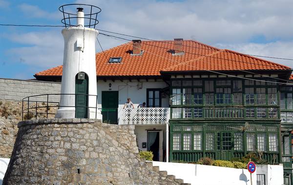 White lighthouse on stone wall beside green glazed house with red tiled roof