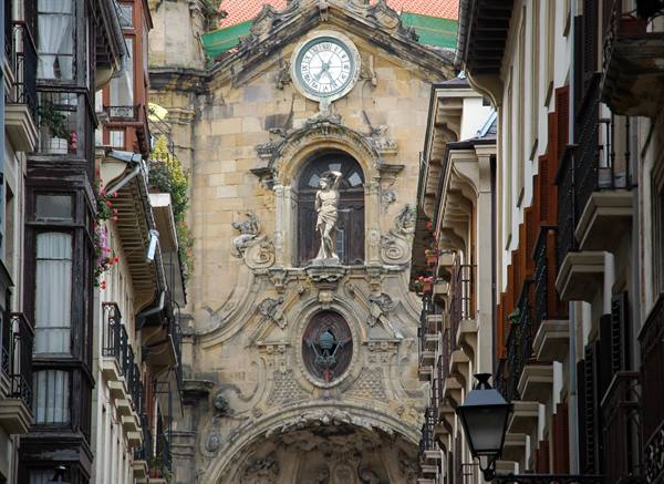 Baroque stone facade with clock and statue between balconies in San Sebastián