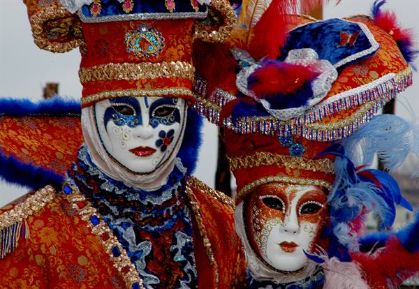 Masks in red and blue costumes with gold trim at Venice Carnival