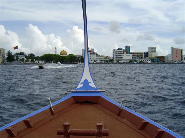 Blue dhoni bow crossing the lagoon, golden dome mosque of Malé behind