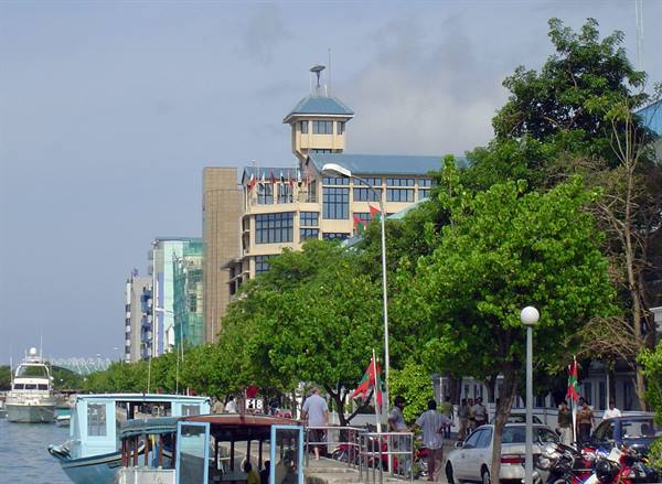 Boat moored on Malé waterfront, traffic and flags under green trees