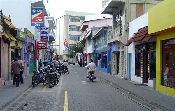 Commercial street with parked bicycles and scooters, colorful shops, people walking