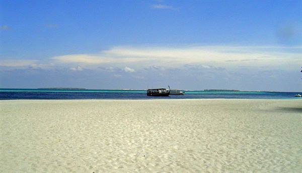 Boat offshore from white sand beach and turquoise water under blue sky