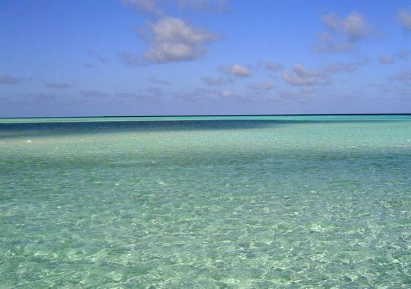 Clear turquoise water over sand, blue sky with scattered clouds