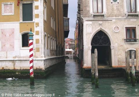 Old buildings facing a Venice canal, with a red and white mooring pole