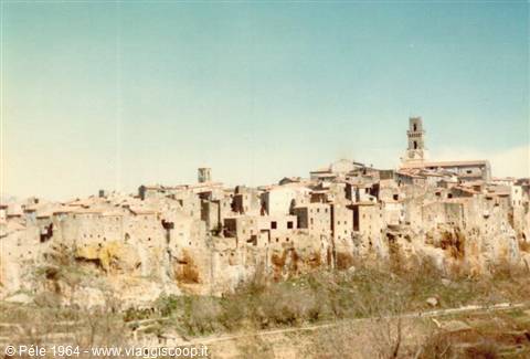 Old tuff houses perched on steep cliff, bell tower rising, clear sky