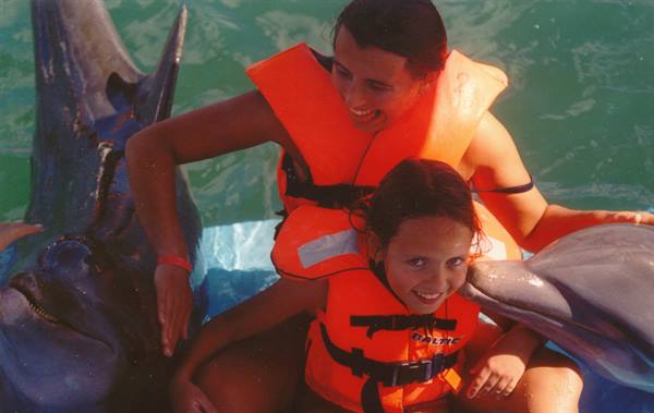 Woman and child in orange life jackets petting dolphins in a pool