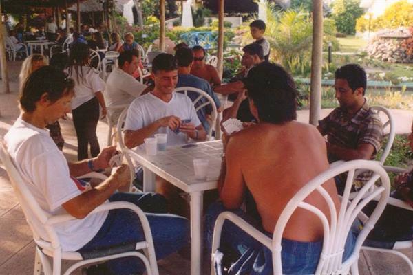 Men playing cards at a white table on a shaded terrace