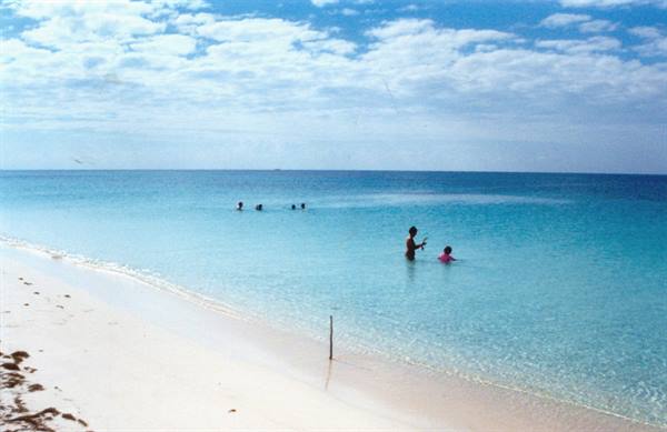 Swimmers in clear turquoise water next to a white sand beach