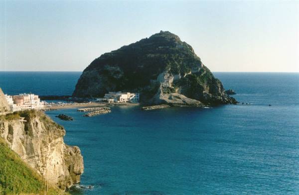 Ischia: green rocky islet on blue sea, white houses and piers near the beach