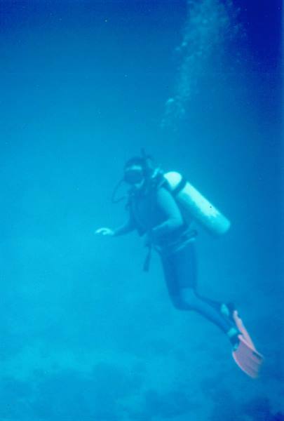 Scuba diver with tank and orange fins swims among bubbles in blue water