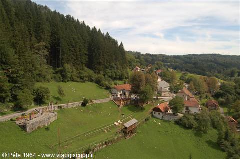 Rural village with church, wooden hayrack and green meadows among forests