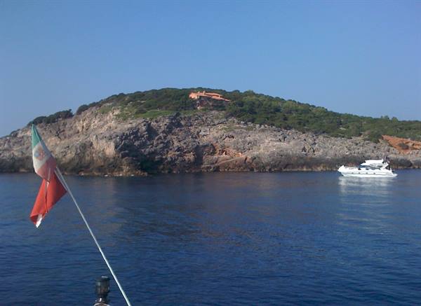 Italian flag on a boat in front of a rocky coast with a white yacht