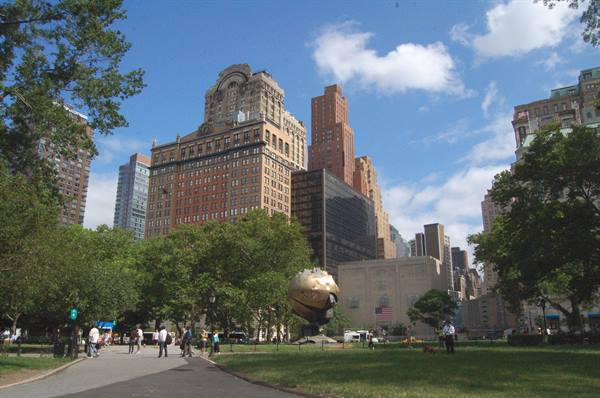 Bronze sphere at Battery Park, New York, people strolling among trees and skyscrapers