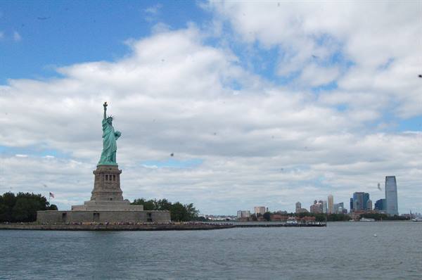 The Statue of Liberty on Liberty Island among clouds, Manhattan skyscrapers on the horizon