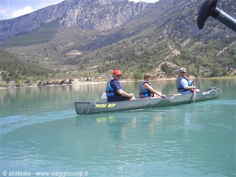 Three people paddling a canoe on turquoise Verdon lake, rocky mountains behind