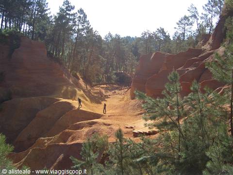 Visitors walk across the ochre cliffs of Roussillon among green pines