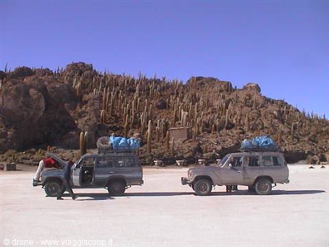 Two loaded 4x4s on white salt flat, cactus island behind, Salar de Uyuni
